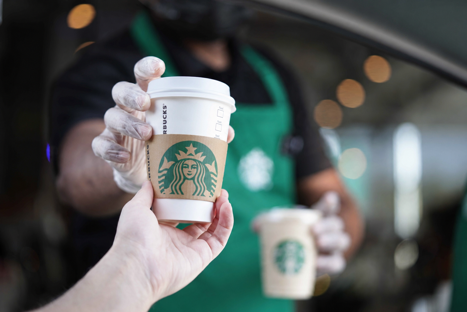 A customer being handed a Starbucks coffee at a drive-thru window